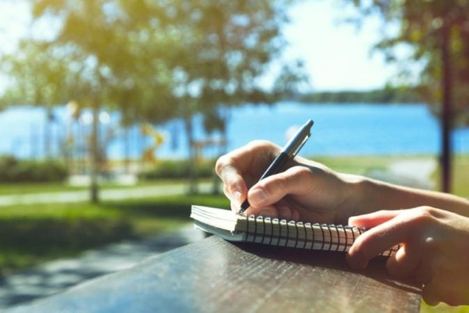 Woman writing a letter by a lake on a summer day