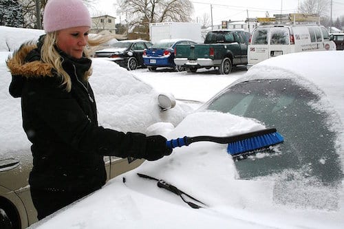 Woman brushing snow off the car window 