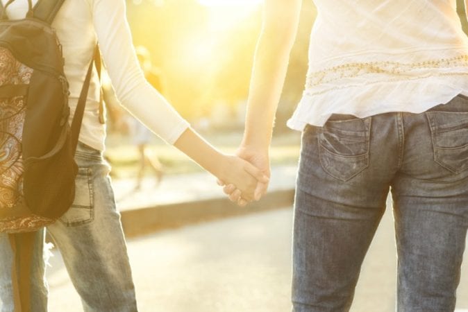 Two women wearing jeans holding hands on college campus