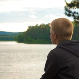 Sad blonde haired boy looking at lake