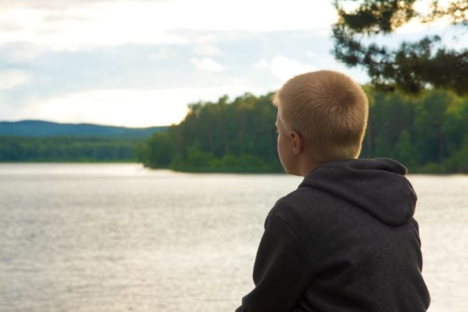 Sad blonde haired boy looking at lake