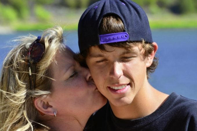 mom kissing teen son on cheek