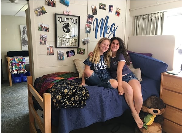 Girls sitting on bed in dorm room.