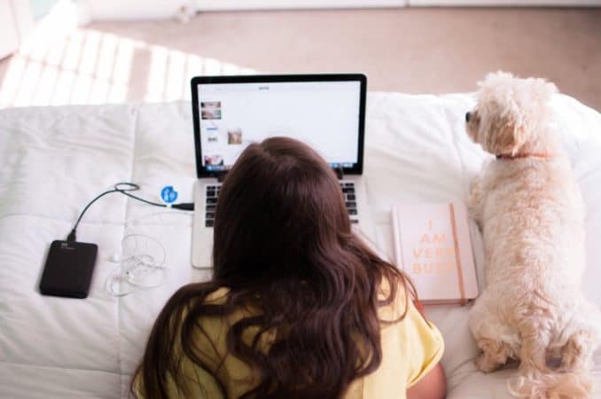 Teen girl on her bed with her laptop and puppy