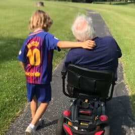 young boy walking with grandfather in wheelchair